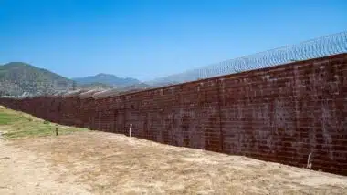 Brick wall with razor wire, correctional facility, prison wall, mountain in background. Barry J. Nidor Juvenile Hall facility, wall, razor wire.