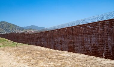 Brick wall with razor wire, correctional facility, prison wall, mountain in background. Barry J. Nidor Juvenile Hall facility, wall, razor wire.