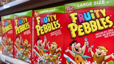 Close-up of multiple Fruity Pebbles cereal boxes on a supermarket shelf.