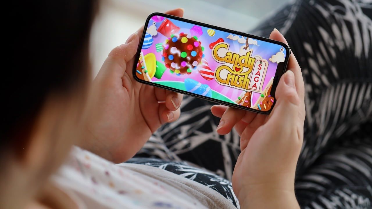 Candy Crush Saga mobile iOS game on iPhone 15 smartphone screen in female hands during mobile gameplay.