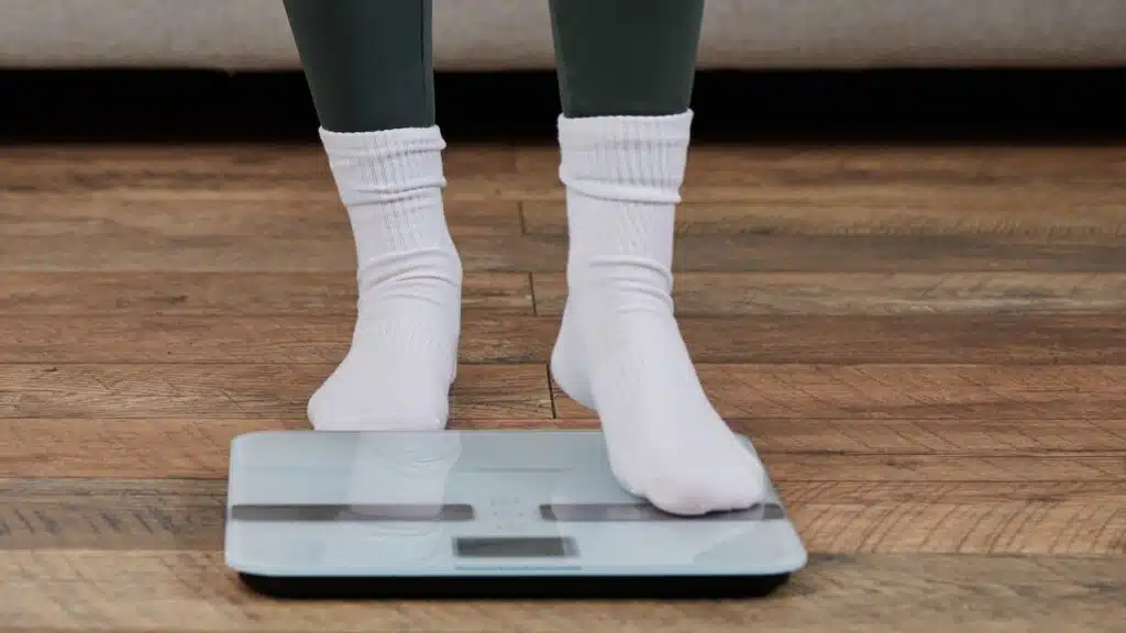 A young woman stands on a scale in her home,