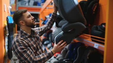 Young father with choosing car seat in store of children's goods.