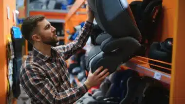 Young father with choosing car seat in store of children's goods.