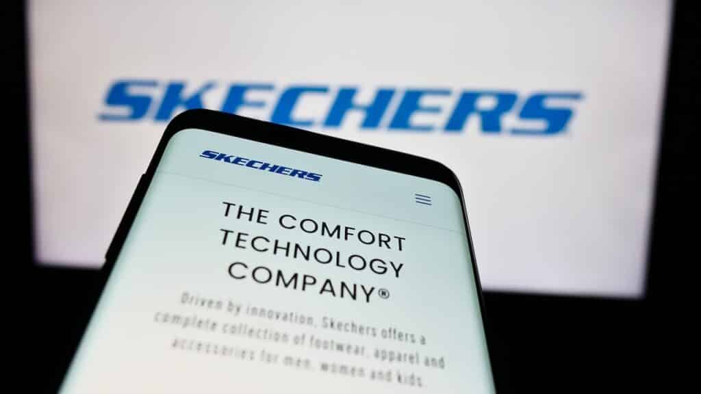 Mobile phone with website of US footwear company Skechers USA Inc. in front of business logo.