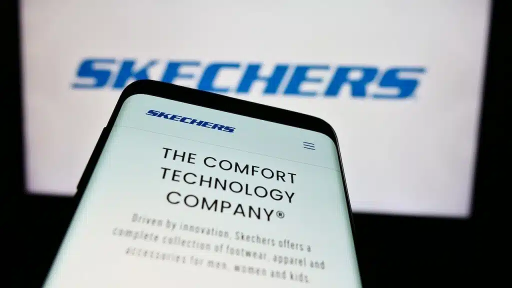 Mobile phone with website of US footwear company Skechers USA Inc. in front of business logo.