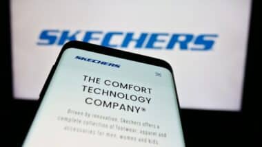Mobile phone with website of US footwear company Skechers USA Inc. in front of business logo.