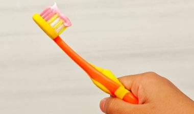 A child's hand holds a toothbrush with toothpaste on it.