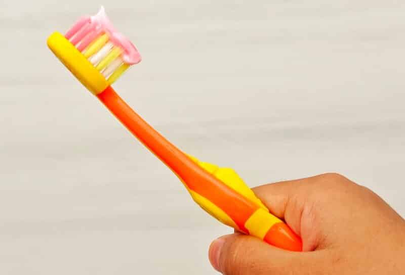 A child's hand holds a toothbrush with toothpaste on it.