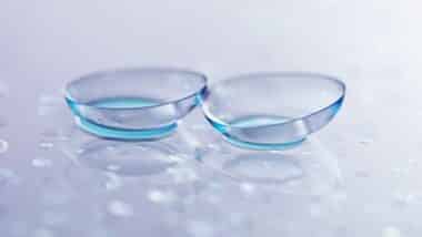 Pair of contact lenses and water drops on light mirror surface, closeup