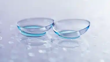 Pair of contact lenses and water drops on light mirror surface, closeup