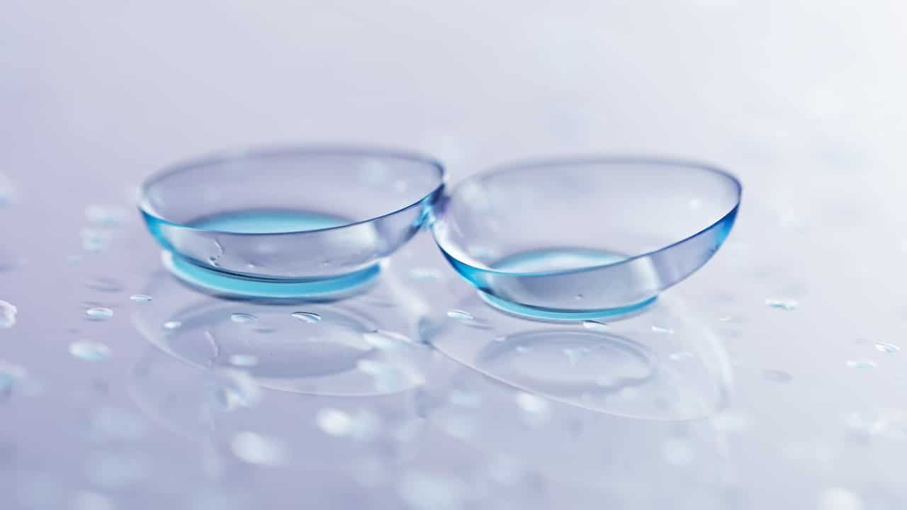 Pair of contact lenses and water drops on light mirror surface, closeup