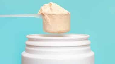 Protein powder in scoop and plastic jar on blue background.