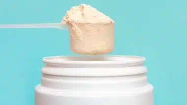 Protein powder in scoop and plastic jar on blue background.