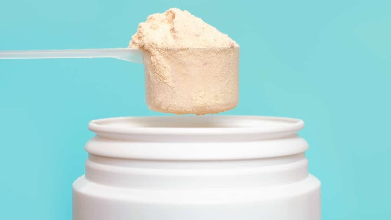 Protein powder in scoop and plastic jar on blue background.