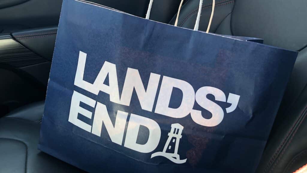 A Lands End brand shopping bag from a retail store sits on a front car seat.