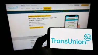 Person holding smartphone with logo of US credit reporting agency TransUnion on screen in front of website