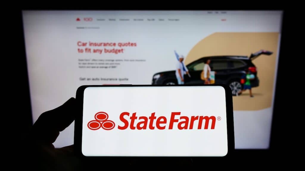 Person holding smartphone with logo of State Farm Mutual Automobile Insurance Company on screen in front of website.