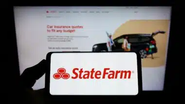 Person holding smartphone with logo of State Farm Mutual Automobile Insurance Company on screen in front of website.