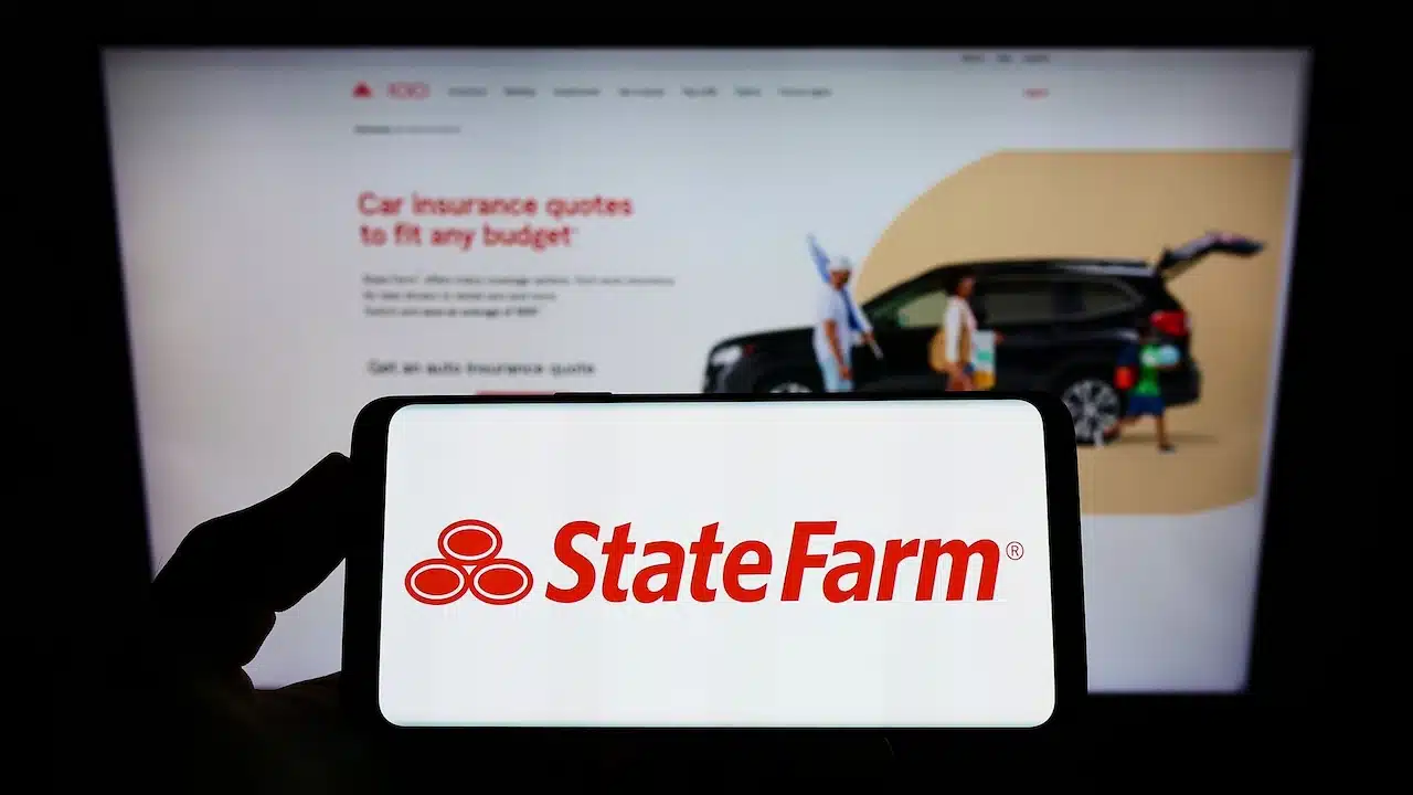 Person holding smartphone with logo of State Farm Mutual Automobile Insurance Company on screen in front of website.