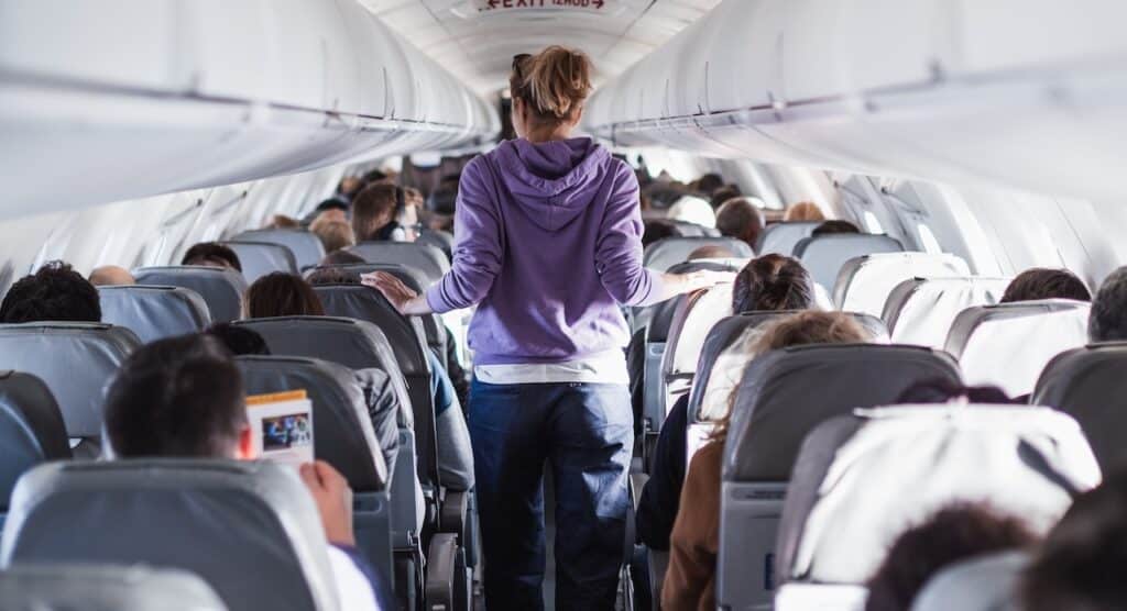 Interior of airplane with passengers on seats and female traveler walking the aisle.