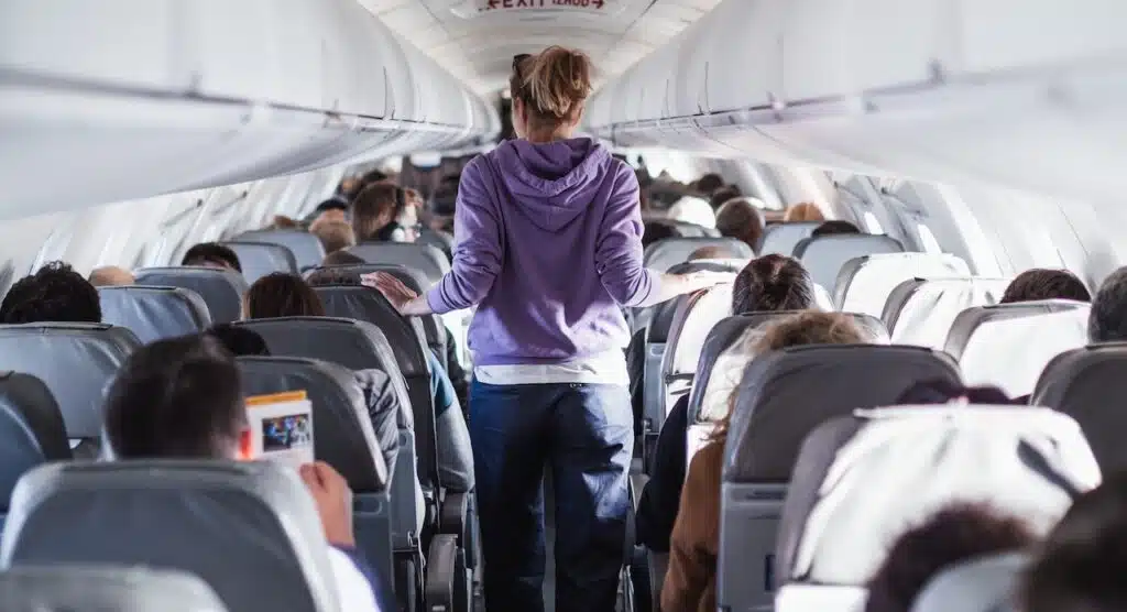 Interior of airplane with passengers on seats and female traveler walking the aisle. 