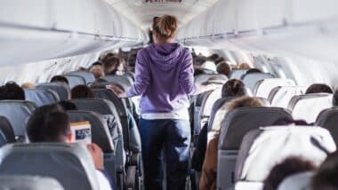Interior of airplane with passengers on seats and female traveler walking the aisle.