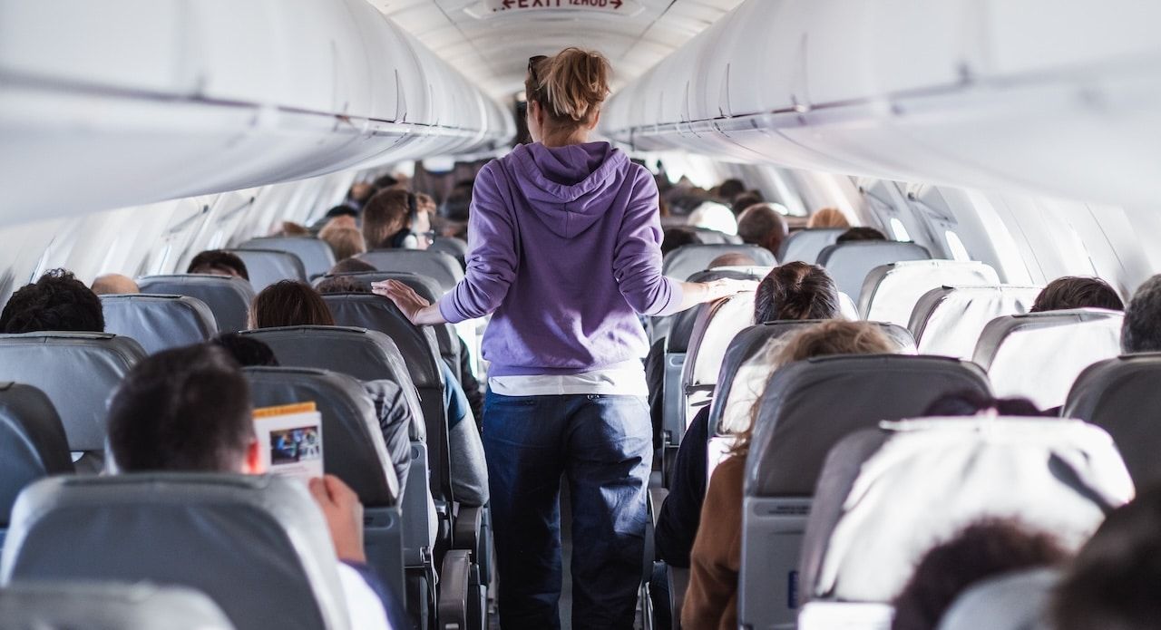 Interior of airplane with passengers on seats and female traveler walking the aisle.