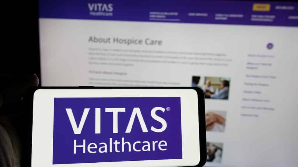 Person holding smartphone with logo of US health care company VITAS Healthcare on screen in front of website.