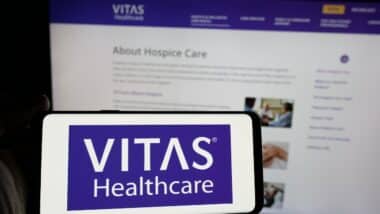 Person holding smartphone with logo of US health care company VITAS Healthcare on screen in front of website.