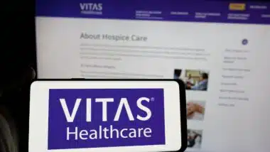 Person holding smartphone with logo of US health care company VITAS Healthcare on screen in front of website.