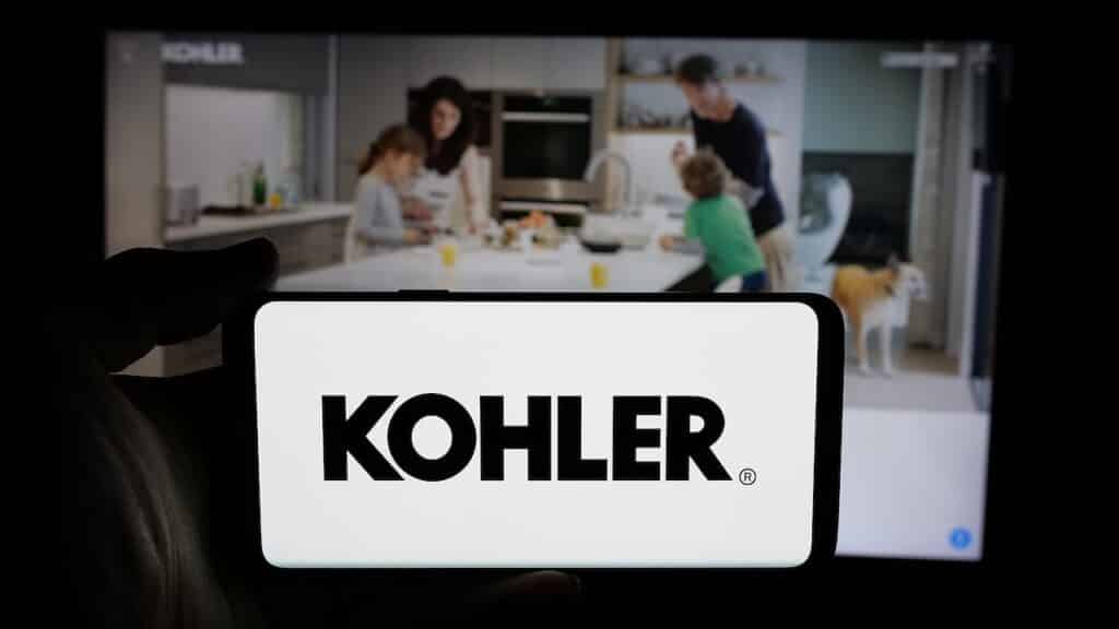 Person holding cellphone with logo of US manufacturing company Kohler Co. on screen in front of webpage.