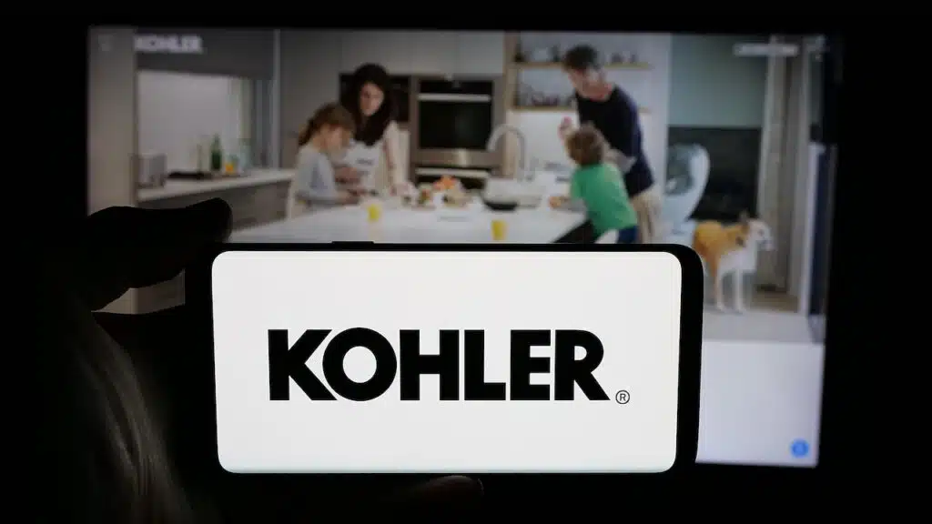 Person holding cellphone with logo of US manufacturing company Kohler Co. on screen in front of webpage.