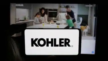 Person holding cellphone with logo of US manufacturing company Kohler Co. on screen in front of webpage.
