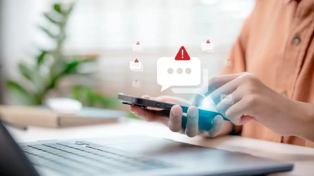 Close-up hand holding smartphone with spam alert icon popping up.