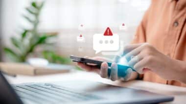 Close-up hand holding smartphone with spam alert icon popping up.