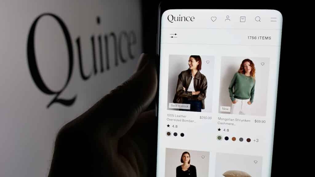 Person holding smartphone with web page of US fashion company Last Brand Inc. (Quince) on screen in front of logo. Focus on center of phone display.
