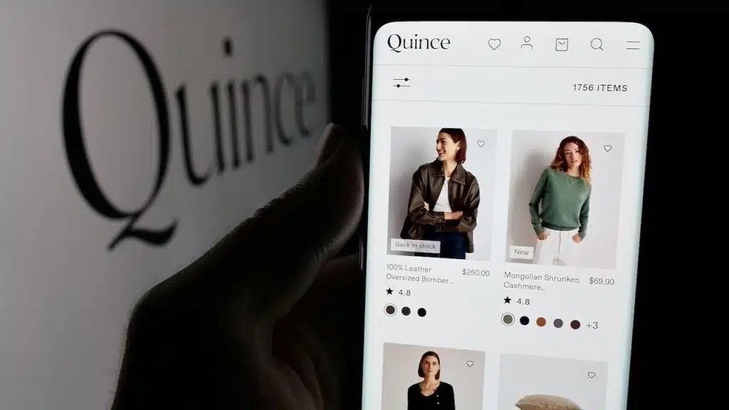 Person holding smartphone with web page of US fashion company Last Brand Inc. (Quince) on screen in front of logo. Focus on center of phone display.