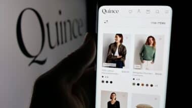 Person holding smartphone with web page of US fashion company Last Brand Inc. (Quince) on screen in front of logo. Focus on center of phone display.