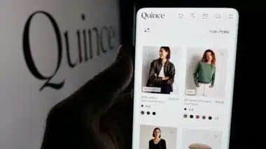 Person holding smartphone with web page of US fashion company Last Brand Inc. (Quince) on screen in front of logo. Focus on center of phone display.