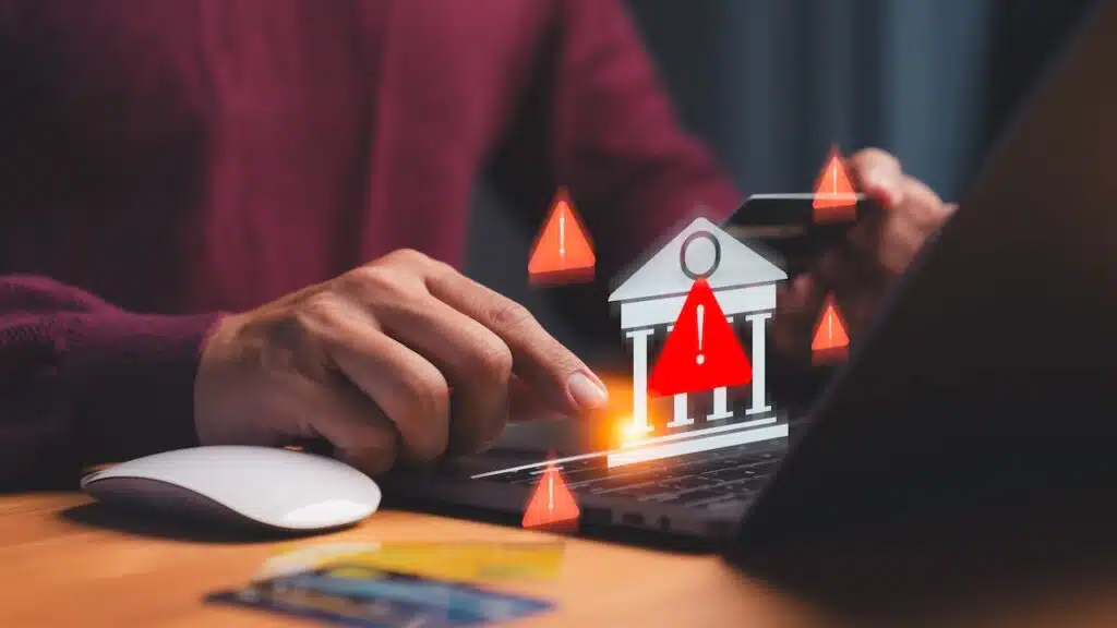 Cybersecurity warning concept showing hand using laptop and credit card with alert icons and bank symbol