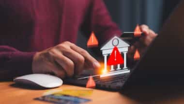 Cybersecurity warning concept showing hand using laptop and credit card with alert icons and bank symbol