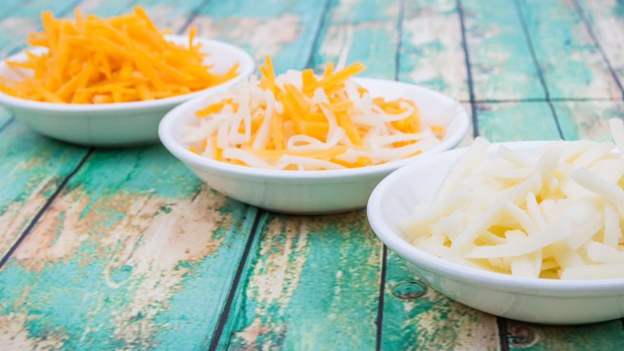 Grated mix mozzarella and cheddar cheese in white bowls over wooden background