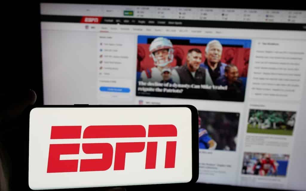 Person holding smartphone with logo of US cable sports television channel ESPN on screen in front of website.
