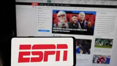 Person holding smartphone with logo of US cable sports television channel ESPN on screen in front of website.
