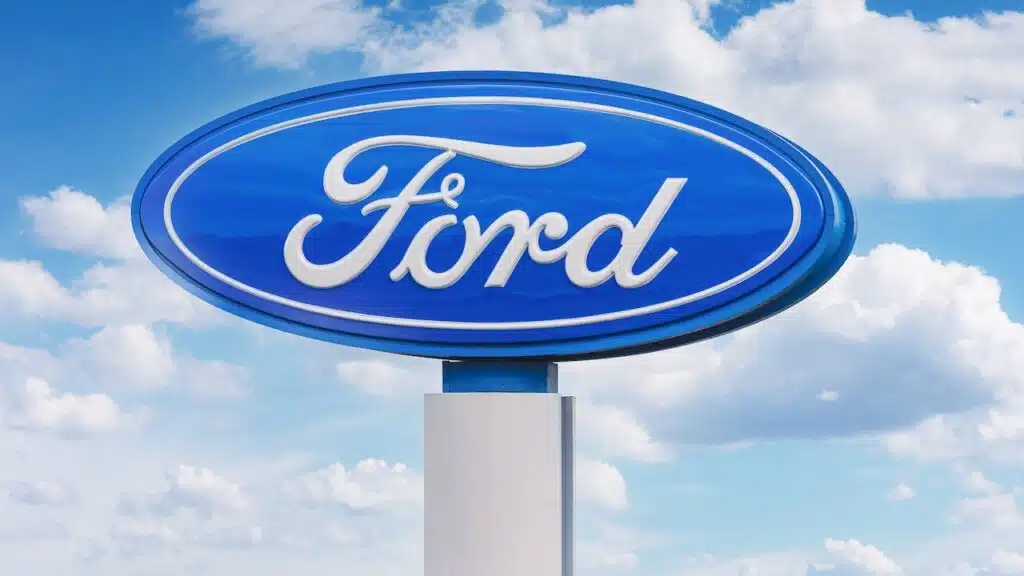 Ford Logo Sign on White Pylon Against Blue Sky and Clouds