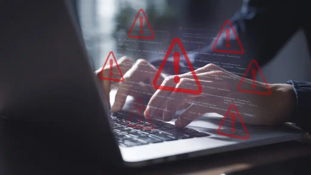 Cybersecurity Alert: Hands Typing on Laptop with Overlay of Code and Multiple Red Warning Signs Indicating System Error or Data Breach Threat