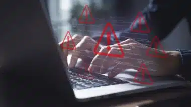 Cybersecurity Alert: Hands Typing on Laptop with Overlay of Code and Multiple Red Warning Signs Indicating System Error or Data Breach Threat