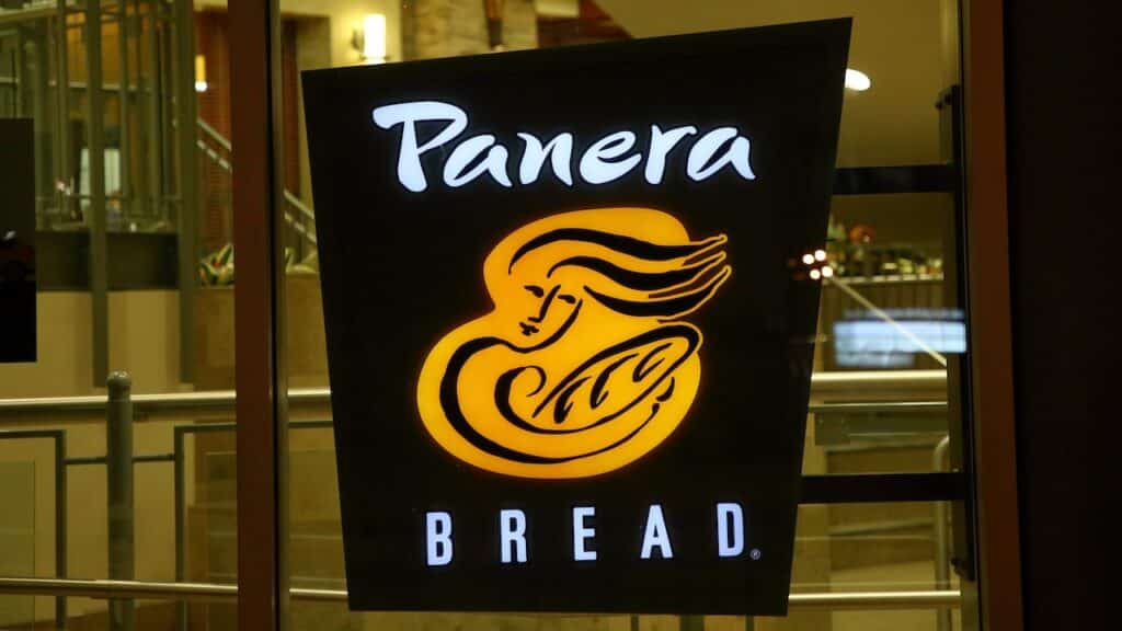 A Panera Bread sign illuminated in the store window.