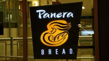 A Panera Bread sign illuminated in the store window.