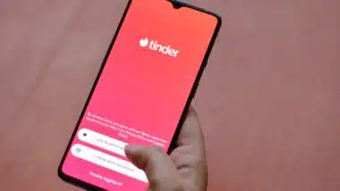 Flat lay with wooden background and Tinder app logo on display on a smartphone screen in female hands.
